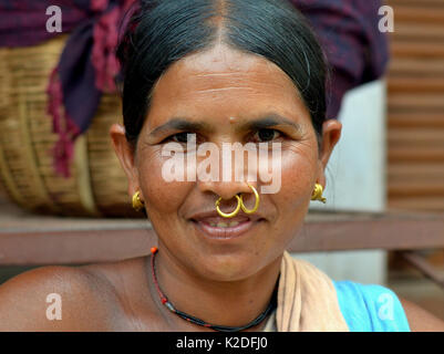 Indian Adivasi woman (Mali tribe) with two golden nose rings and distinctive tribal earrings smiles for the camera. Stock Photo