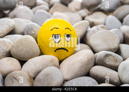 Smiley face made of stone, painted yellow, insulted, lies in between stones Stock Photo