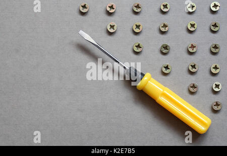 Industrial concept. Yellow screwdriver near lot of screws on gray surface with copy space Stock Photo