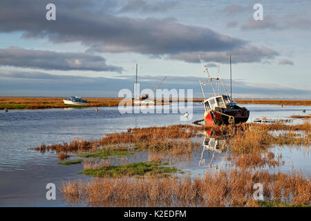 Old boats alongside channel with rising tide,  Dee Estuary,  early morning sunlight near Heswall, Wirral, Merseyside, UK January. Stock Photo