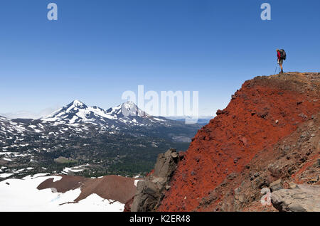 Hiker on the crater rim of Broken Top, and view towards Middle and North Sister. Three Sisters Wilderness, Deschutes National Forest.  Oregon, USA, July 2014.  Model released. Stock Photo