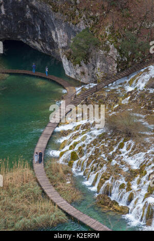 Tourists walking on boardwalk below Velike Kaskade waterfalls, Plitvice Lakes National Park, Croatia. January 2015. Stock Photo
