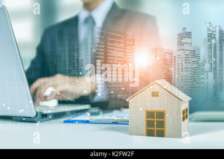 businessman work on laptop with wooden home model, graph and city at night background Stock Photo