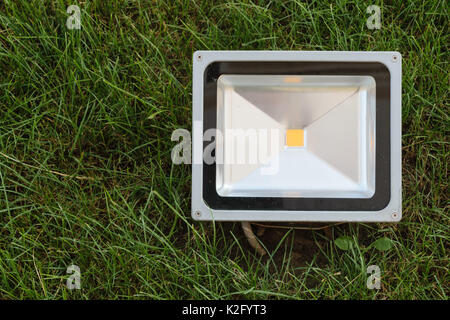 economical LED projector mounted in the green grass. LED spotlight installed in the lawn. Stock Photo
