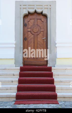 massive wood door, artistic concrete walls and red carpet on stairs entrance Stock Photo