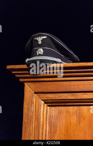 Nazi cap exhibited on wooden wardrobe on black background Stock Photo