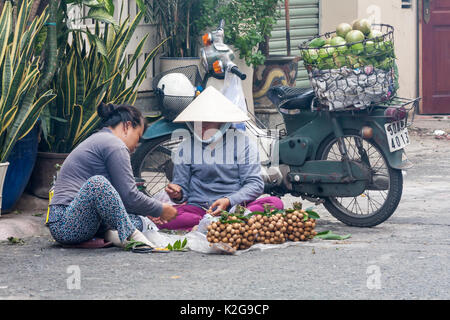 Two fruit vendors bundling longan fruits on the street, Ho Chi Minh City (Saigon), Vietnam Stock Photo