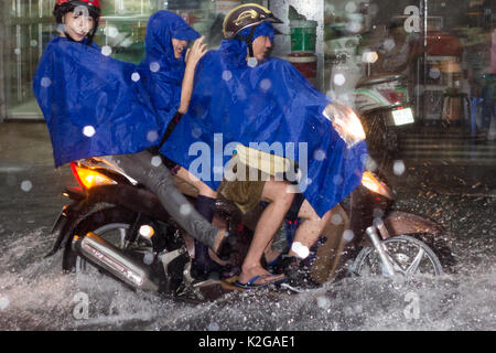 Four people on motorbike driving  through floodwater and torrential rain on Bui Vien street, Ho Chi Minh City (Saigon), Vietnam Stock Photo