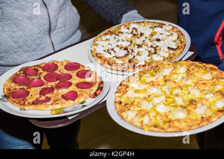 Chef holds with hands white ceramic plates with three hot freshly prepared different pizza with four cheese, moshrooms and salami from a stove of rest Stock Photo
