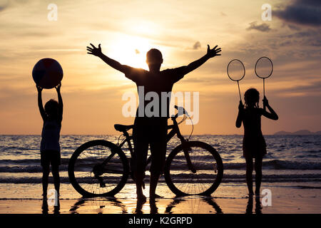 Father and children playing on the beach at the sunset time. Concept of happy friendly family.