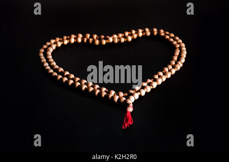 A simple beaded or rosary rests upon a rustic table laid out in the shape of a heart. Symbols of Christ love. Stock Photo