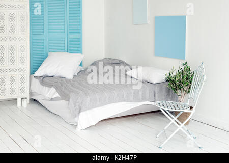 White loft interior in scandinavian style. Cozy area of apartment in nordic style, bedroom with white wood flooring, metal chair and olive tree. Room makeover concept, free space for text. Stock Photo