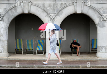 A lady walks with an umbrella along the esplanade on Bournemouth beach in Dorset. Stock Photo