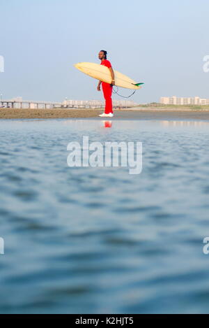 Man holding a surfboard on the beach with calm seaside Stock Photo