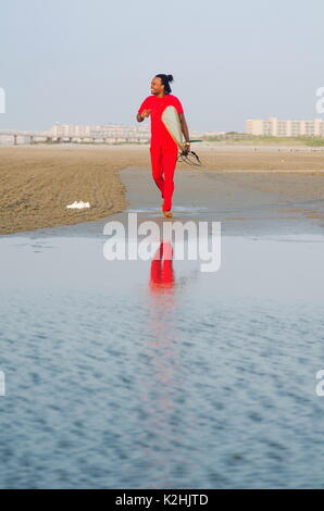 Young man running with a surfboard on the beach Stock Photo