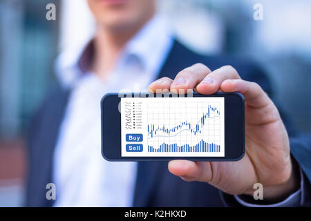 Trader showing smartphone screen with trading interface dashboard with candlestick chart, quotes and buy sell buttons, stock exchange and fintech conc Stock Photo