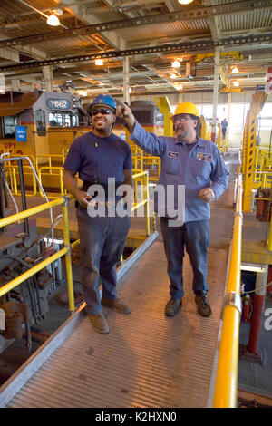 An African American railroad maintenance worker gets work instructions from his Caucasian boss at a railroad freight yard repair shed in Roseville, CA. Note locomotive in background. MODEL RELEASE Stock Photo