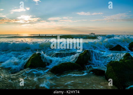 Magnificent morning at the beach with the sun partly hidden behind the clouds and ocean waves on the foreground Stock Photo