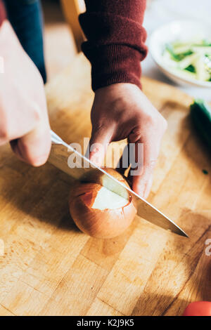 Close up on the hands of young handsome caucasian man cutting onion for dinner - healthy, veggie, food concept Stock Photo