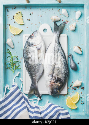 Fresh Sea bream or dorado raw uncooked fish with seasoning on white board over turquoise blue tray background, top view Stock Photo