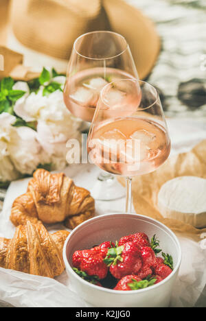 French style romantic summer picnic setting. Flat-lay of glasses of rose wine with ice, fresh strawberries, croissants, brie cheese, hat, sunglasses, Stock Photo