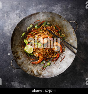 Udon noodles stir-fried with Tiger shrimps and vegetable in wok cooking pan on dark background Stock Photo