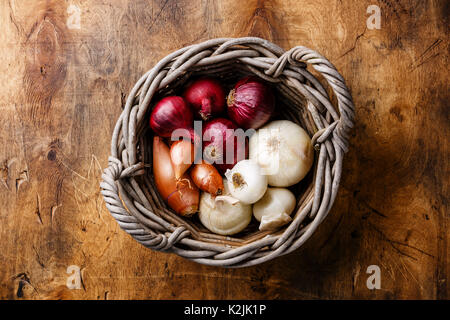 Different types of onions in basket on wooden background Stock Photo