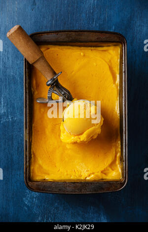 Sorbet mango ice cream ball in scoop on blue background Stock Photo