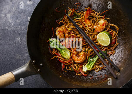 Udon noodles stir-fried with Tiger shrimps and vegetable in wok cooking pan close-up Stock Photo