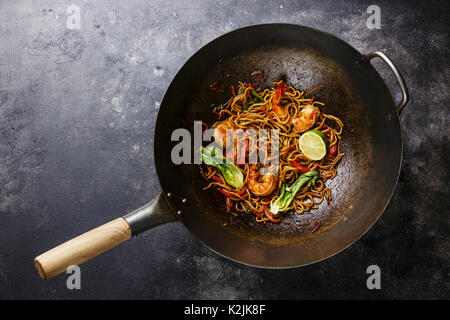 Udon noodles stir-fried with Tiger shrimps and vegetable in wok cooking pan on dark background Stock Photo