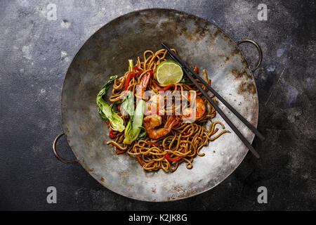 Udon noodles stir-fried with Tiger shrimps and vegetable in wok cooking pan on dark background Stock Photo