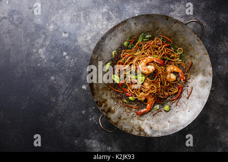 Udon noodles stir-fried with Tiger shrimps and vegetable in wok cooking pan on dark background copy space Stock Photo