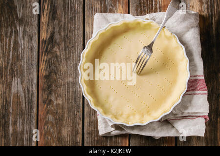Dough for baking quiche tart in ceramic baking form ready for bake on kitchen towel over old plank wooden background. Flat lay with copy space Stock Photo