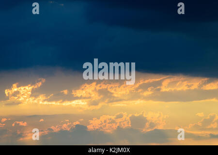 After a violent thunderstorm, at the top dark rain clouds, below a warm sunset Stock Photo