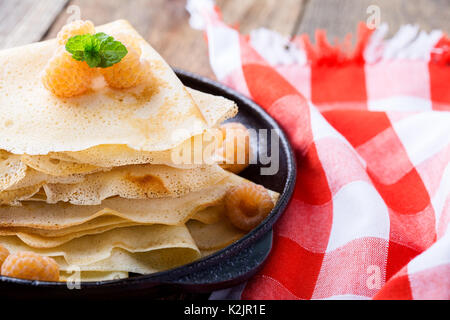 Homemade  crepes served with fresh yelllow raspberries  in cast iron skillet for romantic brunch on rustic table witn red-checked tablecloth Stock Photo