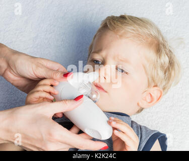Mother using baby electric nasal aspirator. She is doing a mucus suction to twenty months baby boy. Stock Photo