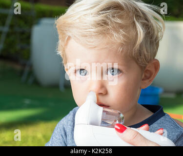 Mother using baby electric nasal aspirator. She is doing a mucus suction to twenty months baby boy,outdoor. Stock Photo