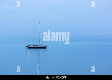 Lonely Black sailing boat in the ocean before sunrise, reflections in blue hour Stock Photo