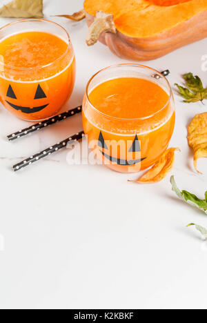 Ideas for a children's and party of Halloween treats. Pumpkin orange cocktail in glasses, decorated with a pumpkin jack lantern, on a white marble tab Stock Photo
