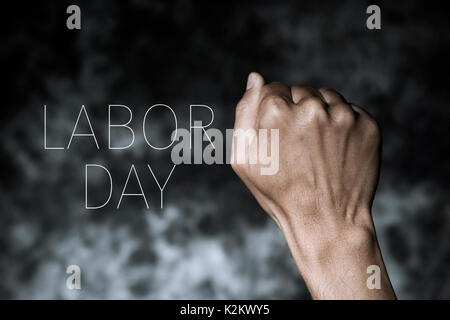 closeup of the raised fist of a young man against a gradient dark gray background and the text labor day Stock Photo