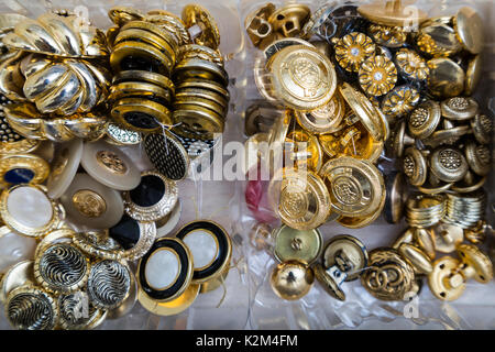 Close up of a collection of gold, silver and metal antique vintage buttons with different patterns in plastic containers in an sewing studio. Stock Photo