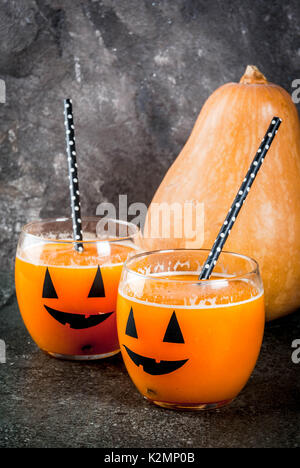 Ideas for a children's and party of Halloween treats. Pumpkin orange cocktail in glasses, decorated with a pumpkin jack lantern, on a black stone tabl Stock Photo