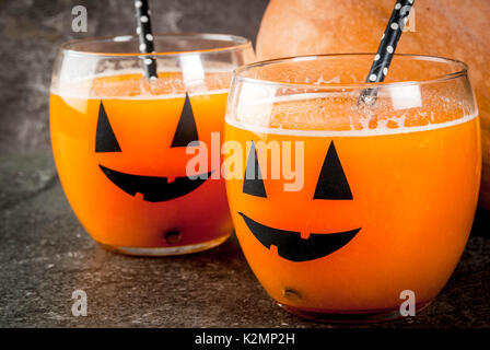 Ideas for a children's and party of Halloween treats. Pumpkin orange cocktail in glasses, decorated with a pumpkin jack lantern, on a black stone tabl Stock Photo
