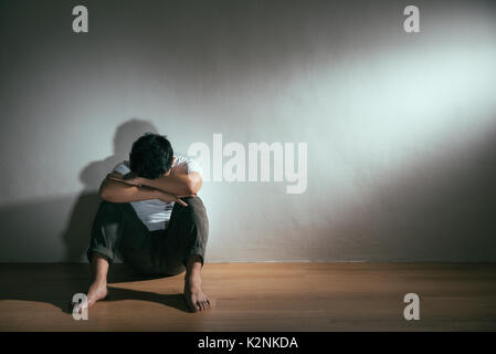 depressed man having autistic intellectual disability sitting on wooden floor crying feeling sadness in dark with white background. Stock Photo