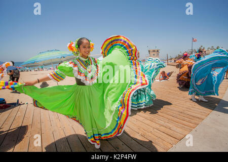 Their folk costumes billowing, smiling teenage Mexican folkloric dancers perform on the Main Beach Boardwalk in Laguna Beach, CA. Stock Photo