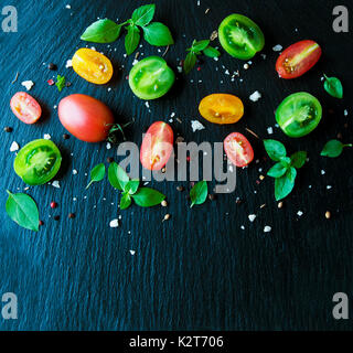 colored slices of tomato with basil and spices on black stone background selective focus, space for text Stock Photo