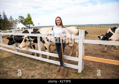 Happiness girl feeding cows on a farm. Young adult freckled girl feed cow on a village field in autumn and play with animals, friendship with cow. Fun Stock Photo