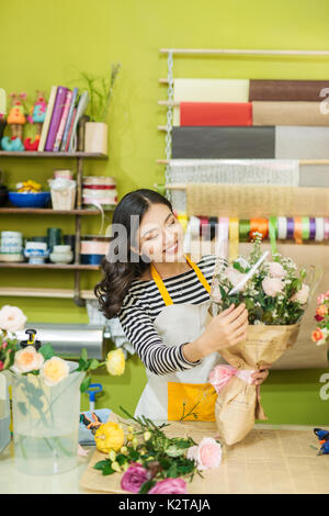 Beautiful young female florist is standing in flower shop and holding bouquet of flowers Stock Photo