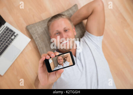 Young Happy Man Lying On Floor Taking Selfie With Mobile Phone Stock Photo