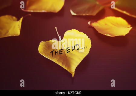 yellow leaf with the inscription the end on the black wood background. Fallen autumn leaf in shape of heart Stock Photo